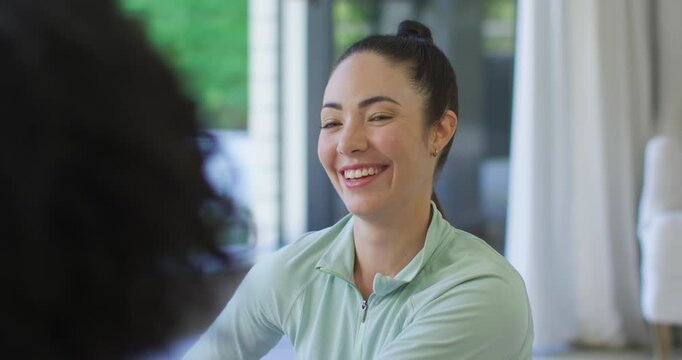 Woman with friend chatting at living room windows, wearing mint top and laughing after funny remark