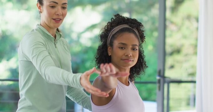 Woman coach speaking hands guiding African American woman client holding right arm in room aligning