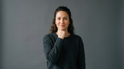 Obraz premium Confident mid-adult woman smiling while resting her chin on her fist, posed against a solid dark gray studio background under soft professional lighting for branding and corporate headshots.