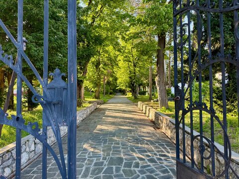 Open old metal gate in front of a tree lined stone path in a church yard in the afternoon sun in Zagreb, Croatia