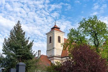 Prostejov, Czech Republic - April 18, 2026: Historic church tower framed by trees under dramatic cloud-filled blue sky, ulice Olomoucka © Professional Art