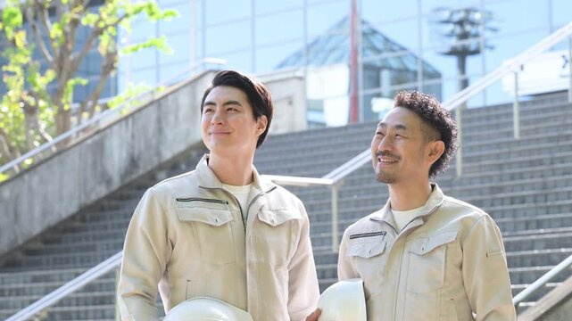 ヘルメットを持つ作業員のポートレート メンテナンスやゼネコンのような建設現場と成長、ビル背景で見上げる作業着の2人のスローモーション動画
