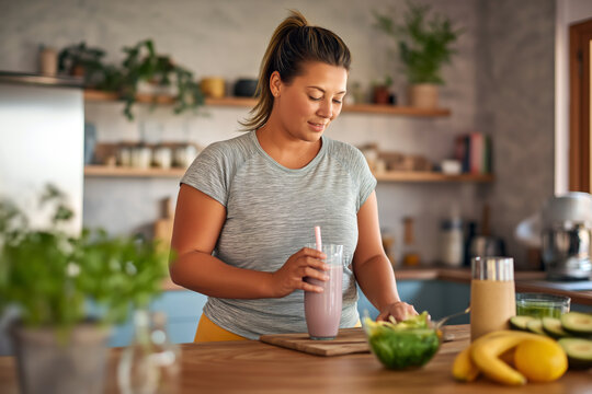 Plus size woman preparing healthy smoothie in kitchen, post workout nutrition, wellness lifestyle