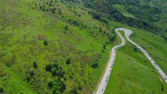 aerial shot captures a scenic, winding mountain road snaking through the vibrant, verdant landscapes of Andorra. The footage showcases the natural beauty of the Pyrenees, with lush green hills, scatte