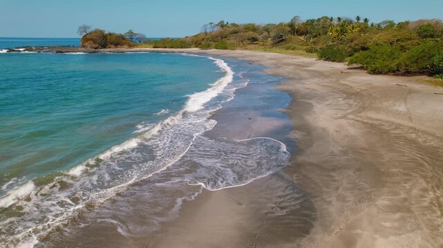Sandy bay with gentle waves reaching an untouched tropical beach in Costa Rica