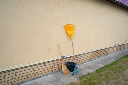 yellow rake, garden pruners and bucket by the wall of the house, garden tools