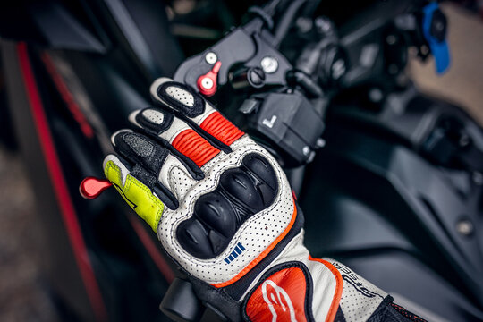Close-up of a motorcyclist&rsquo;s gloved hand gripping the brake or clutch lever, featuring protective sport riding gloves with reinforced knuckles and enhanced grip. The image highlights control, safety