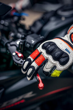 Close-up of a motorcyclist&rsquo;s gloved hand gripping the brake or clutch lever, featuring protective sport riding gloves with reinforced knuckles and enhanced grip. The image highlights control, safety
