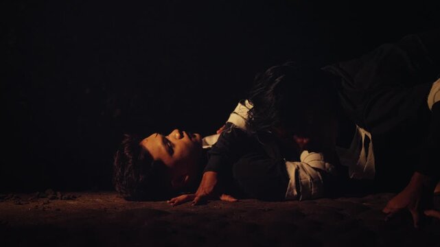 In a dark and gritty setting, one man leans menacingly over another lying on the ground. A dramatic, suspenseful, and intense scene evoking horror or conflict.