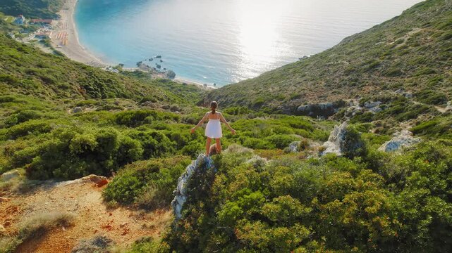 Woman in white dress overlooks lush cliffs and Ionian Sea in Kefalonia, Greece