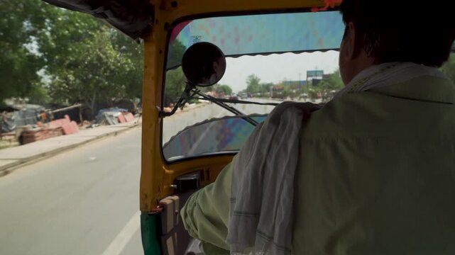 Auto rickshaw driver on sunny road seen from inside tuk tuk