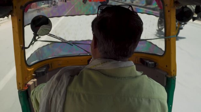 Auto rickshaw driver on sunny road seen from inside tuk tuk