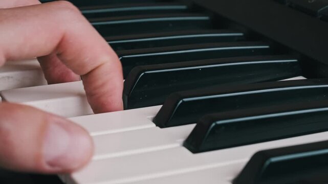 Close-up of a musician hand playing chords and a melody on the black and white keys of a digital piano. This clip shows musical skill, practice, performance, and the art of composing music.