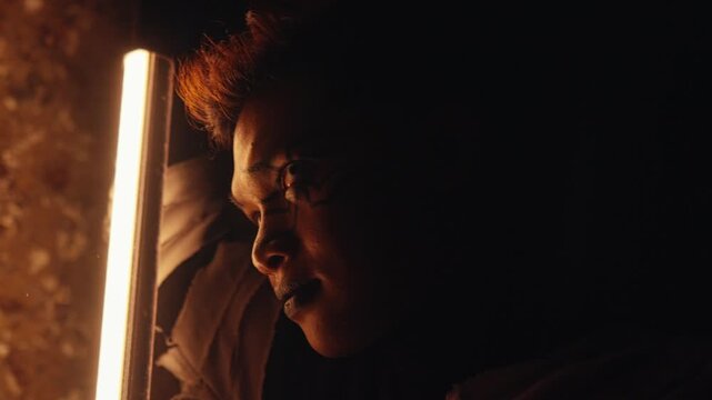 A cinematic close-up of a man's profile in a dark room, with his face partially lit by a single vertical light source. The mood is tense, dramatic, and filled with suspense.