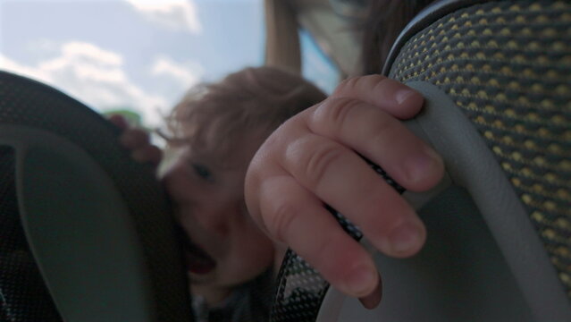 Close-up of toddler&rsquo;s small hands gripping bus seat while peeking playfully between headrests during travel, showing child&rsquo;s curiosity and tactile engagement