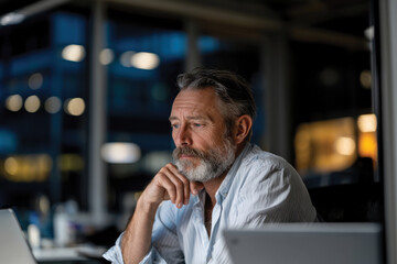 Obraz premium An older man with a thoughtful expression sits in a modern office, embodying wisdom and experience, while reflecting on significant decisions in his professional journey.