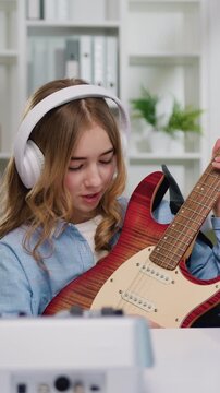 Beautiful preteen female blogger recording video class tutorial for play electric guitar on modern smartphone at home studio. Girl showing how play for electric guitar for internet auditory. Slow