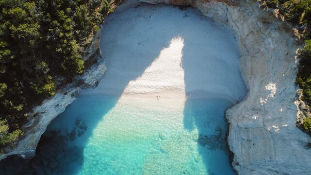 Aerial view of hidden cove with woman lying on white sandy beach turquoise water and lush greenery in summer