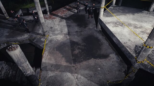 A high-angle wide shot of a group dressed in black walking through a derelict, unfinished concrete building at night, creating an eerie, post-apocalyptic, and dystopian atmosphere.