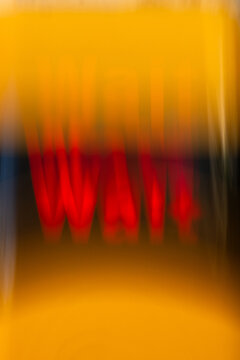 Abstract image with partially blurred word &ldquo;WAIT&rdquo; on yellow background. Selective clarity of the last letter improves readability while motion blur conveys delay, anticipation, uncertainty