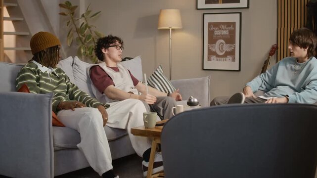 Medium shot of three young adult friend chatting and smoking hookah while spending spare time in living room at home