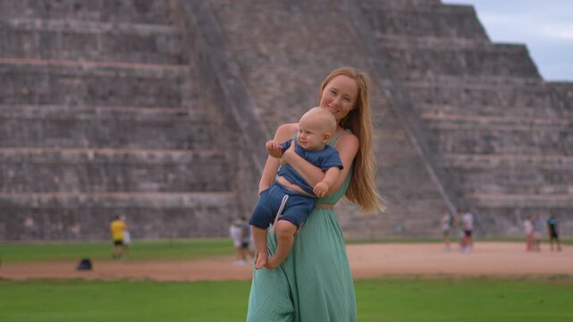 Young mother traveler standing with her one year old son in front of Kukulkan pyramid in Chichen Itza, Mexico. Family travel, motherhood, bonding and cultural tourism concept.