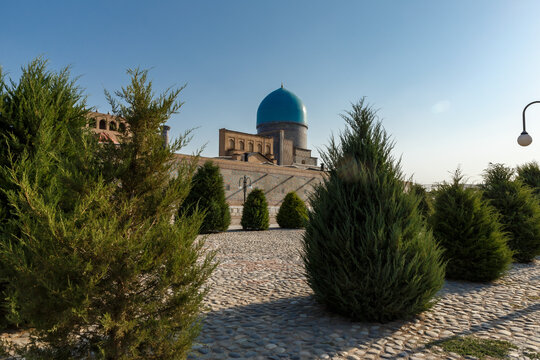 Turquoise dome of Tilla Kari Mosque in Samarkand Uzbekistan seen through green park trees