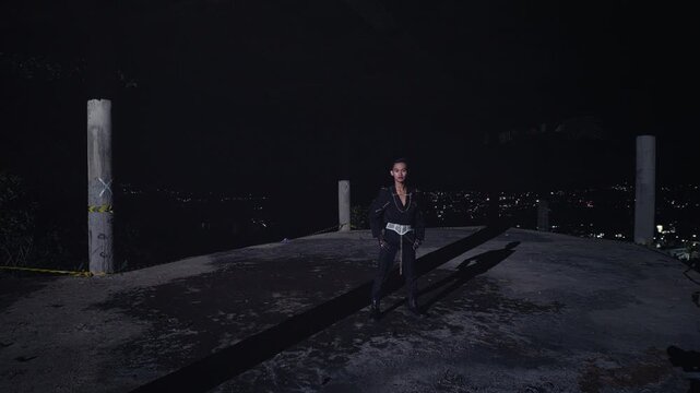 A wide shot of a stylish, androgynous model in a black outfit standing powerfully on an abandoned rooftop, with the city lights blurred in the background. A symbol of urban strength and solitude.