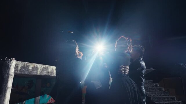 A group performs a strange ritual around a central figure, illuminated by a harsh backlight. The camera dramatically pulls back to reveal their isolation in a vast, derelict building at night.