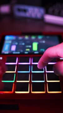Close-up of a hand pressing vibrant glowing pads on a red electronic beatmaker with colorful lights changing dynamically. This action captures the essence of music production.