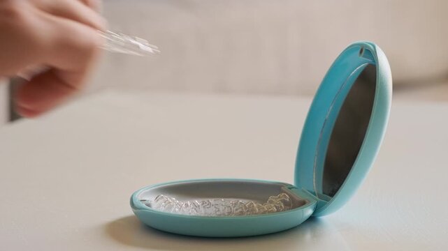 Close-up view of hands opening protective case and taking dental aligner. Dental care, orthodontics, bite or occlusion correction, teeth straightening, personal hygiene accessories
