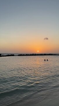 Golden sunset over Mambo Beach with swimmers