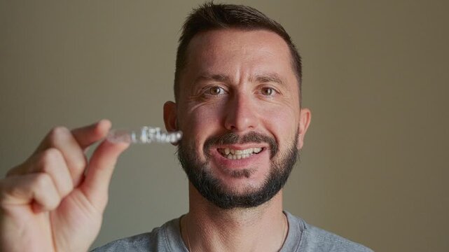 Portrait of man holding transparent dental aligner in front of his face. Orthodontic treatment, bite correction, occlusion correction, teeth straightening, dental care