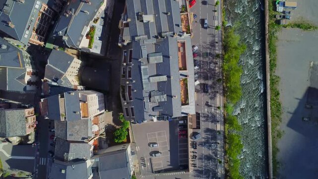 An aerial drone shot showcasing the charming cityscape of Andorra, with traditional buildings nestled alongside a winding river. The footage captures the unique architectural style and the natural bea