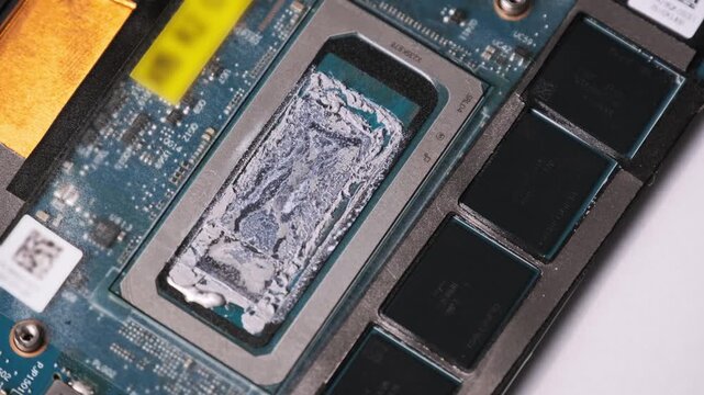 A rotating close-up shows a processor chip covered in dry thermal paste on a green motherboard with memory modules. Concept of hardware maintenance, computer repair, and thermal management.