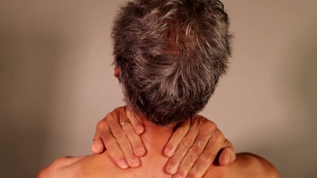 Senior Man in pain doing a self-massage on his upper back neck and shoulders
