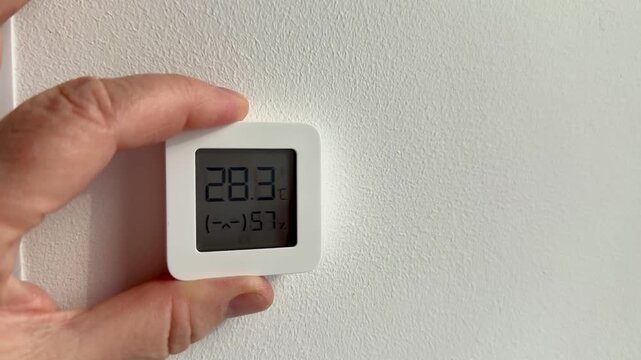 Hand mounts digital sensor on textured wall showing and humidity closeup of woman's hand placing compact white device homeowner
