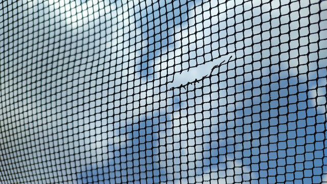 Black plastic mesh netting featuring a small tear or hole. Ideal for showing repair needs, damage assessment, or maintenance for window screens and garden nets.
