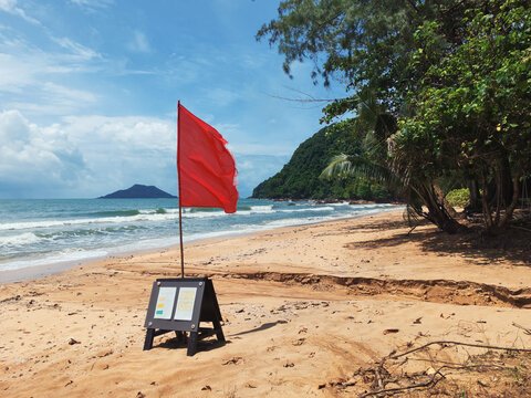 Red warning flags flying on a sandy beach during a windy day with waves