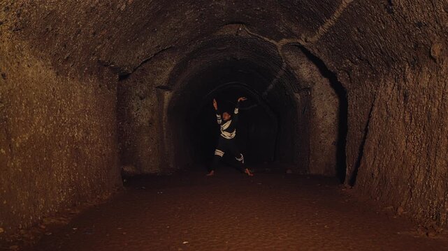 In the depths of a dark, earthen tunnel, a lone warrior performs a powerful, ancient dance with a rope whip. His focused movements evoke a sense of spiritual ritual, tradition, and immense energy.
