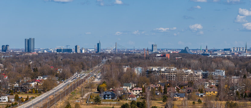 Aerial view of Riga, Latvia, with a construction corridor toward the skyline, Riga TV Tower, National Library of Latvia, high rises, houses, leafless trees, and machinery.