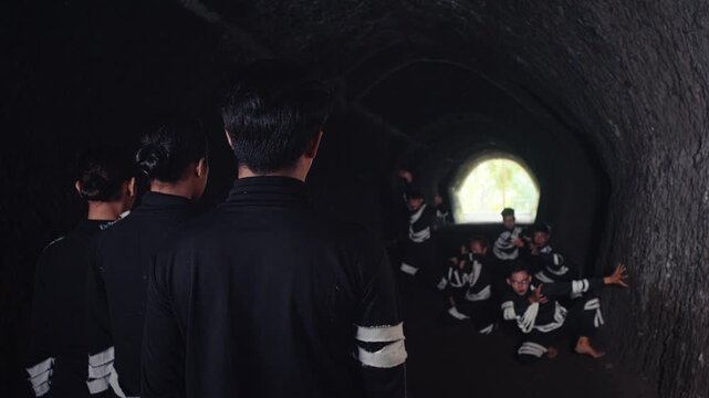 An over-the-shoulder shot shows a group watching fellow performers dance and celebrate at the bright exit of a dark tunnel. A conceptual video about reaching a goal, freedom, and community.