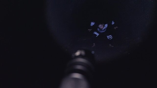 A terrifying first-person POV shot of exploring a dark cave with a flashlight. The beam lands on a woman in a costume who performs a frantic and scary dance, like a monster or ghost.