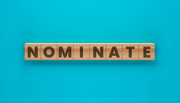 Nominate Wooden Block Lettering: A top-down shot of the word NOMINATE meticulously spelled out using individual wooden blocks, presented against a striking and minimalist backdrop.