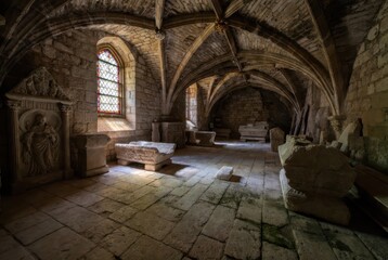 Fototapeta premium Ancient Stone Crypt with Stained Glass Window and Carved Sarcophagi in Dim Light