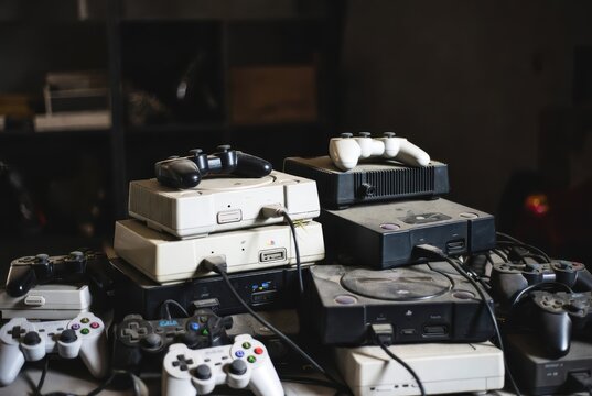 Vintage gaming consoles and controllers stacked, dusty, and ready for retro fun.