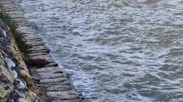 Murky Water Waves with White Foam Hitting Stone Embankment