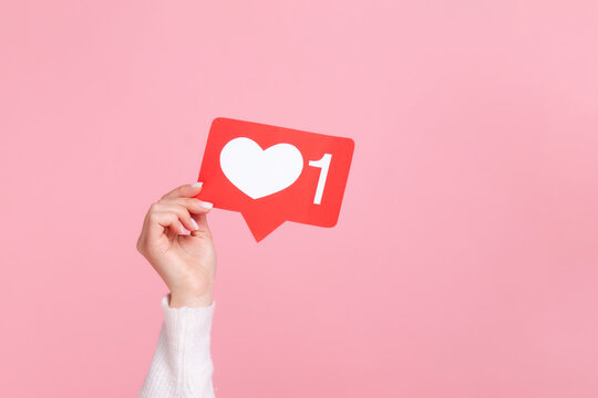 Hand holding red social media like notification icon for online popularity or marketing isolated over pink background with copy space