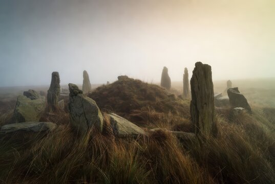 Ancient Standing Stones in Misty Moorland Landscape at Sunrise with Golden Light