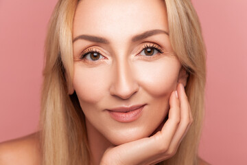 Fototapeta premium Close up portrait of middle aged woman with clean skin for anti-aging cosmetic therapy demonstration isolated on pink background
